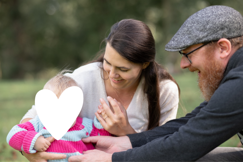Foto einer dreiköpfigen Familie. Mann und Frau schauen zum Kleinkind und interagieren mit ihm und halten es fest