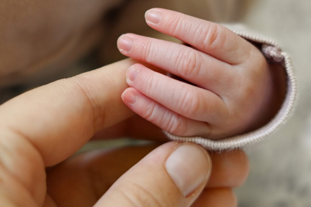 Foto einer Hand von einem Neugeborenen Baby. Im Größenvergleich sieht man die Hand einer erwachsenen Person