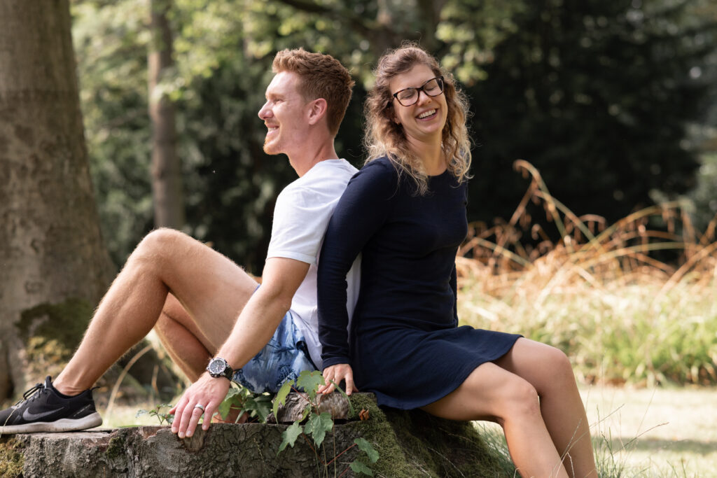 Foto eines Paares. Mann und Frau sitzen auf einem Baumstamm. Sie sind Rücken an Rücken aneinander gelehnt.