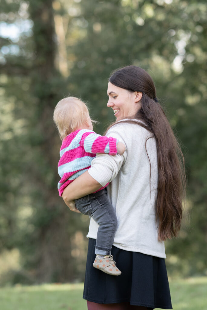 Mama hält ihr Kleinkind auf dem Arm und hat dem Fotografen den Rücken zugewandt