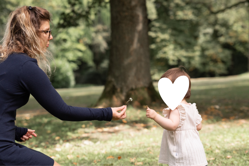 Foto einer Frau und eines Kleinkindes. Die Frau hält dem Kleinkind eine Blume hin