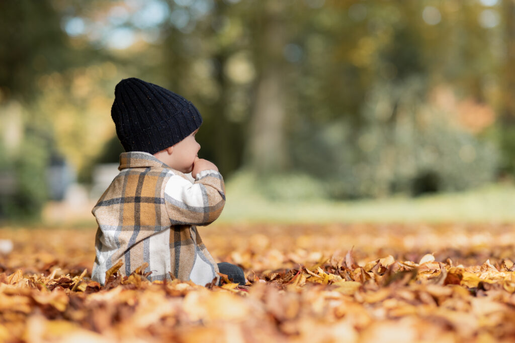 Foto eines kleinen Kindes im Herbstlaub. Das Kind trägt eine Mütze und man sieht den Rücken.