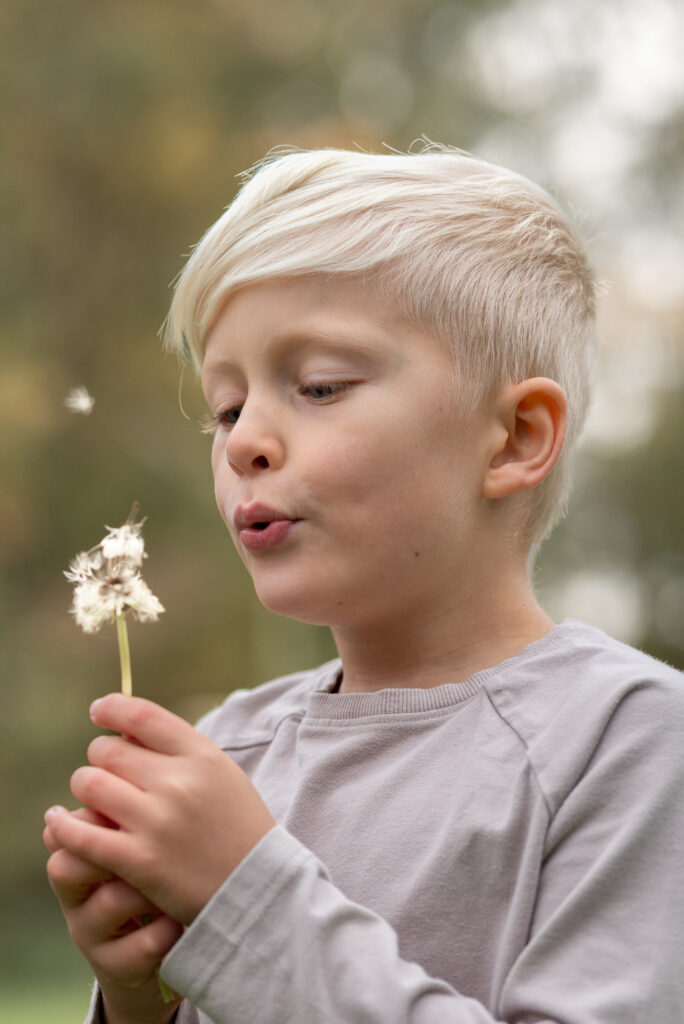 Foto eines Jungen, der eine Pusteblume pustet