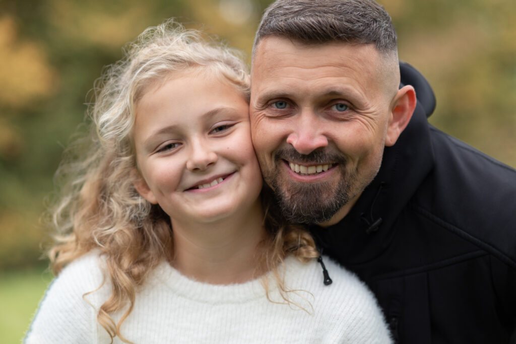 Foto von Papa und Tochter. Beide Gesichter sind Wange an Wange und schauen in die Kamera