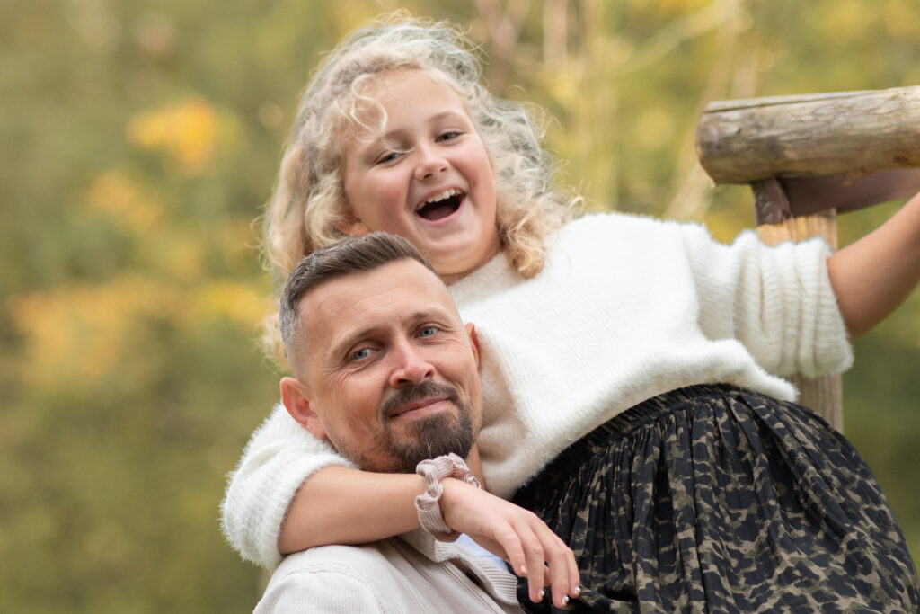 Foto von Vater und Tochter. Vater hebt Tochter hoch und beide lachen in die Kamera
