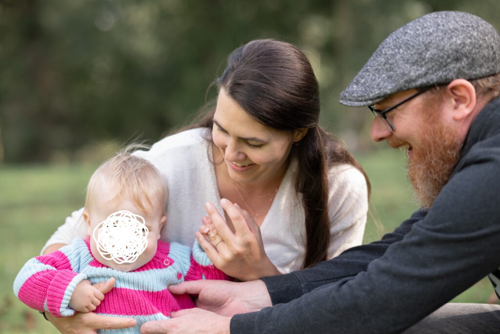 Bild einer dreiköpfigen Familie. Mama und Papa halten das Kind und interagieren mit ihm, halten es fest und kitzeln