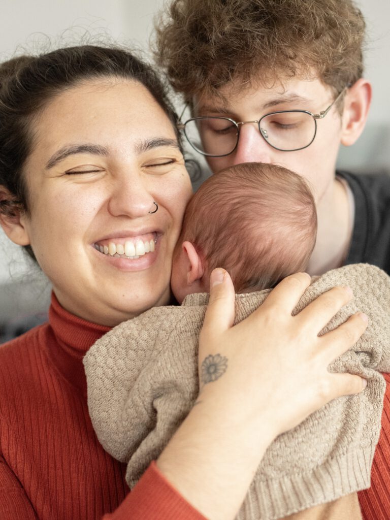 Bild einer dreiköpfigen Familie. MAma und Papa halten das Neugeborene im Arm. Buche dein Fotoshooting in Mönchengladbach
